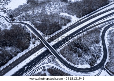 Drone shot of an empty asphalt freeway crossing through cold snowy woods during winter time