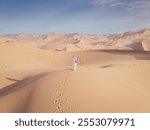 Drone shot of the girl walking on the super dunes of Kumtag desert in Northwestern China near ShanShan, one of the hottest regions worldwide.