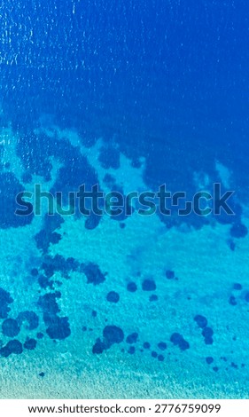 Drone shot looking straight down onto a mesmerizing clear blue sea surface revealing distinct isolated dark rocky patches resting peacefully on the sandy seabed.