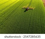 Drone shot of a red tractor applying treatment to wheat crops in vast farmland