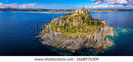 Drone shot of St Michael’s Mount in Cornwall, showing historic castle, marina, and lush greenery. Great for travel, tourism, heritage, island life, and coastal destination themes