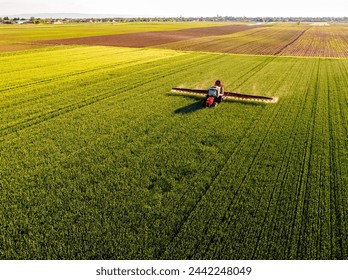 Drone shot of a tractor with sprayer in action on a vibrant green wheat farmland - Powered by Shutterstock