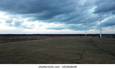 Drone Shot Of Turbulent Windmills Preparing For A Upcoming Storm Standing On A Dry Field With A Treeline In The Background, Presenting Climate Change - Kirstalpark Lommel