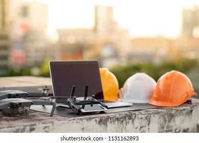 Drone, smartphone, laptop computer and protective helmet at construction site. Using unmanned aerial vehicle (UAV) for land and building site survey in civil engineering project.
