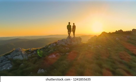 DRONE, SUN FLARE: Cinematic Shot Of Active Young Couple Observing The Evening Landscape After Hiking In The Green Mountains Of Slovenia. Idyllic Morning Sunbeams Shining On Male And Female Trekkers.