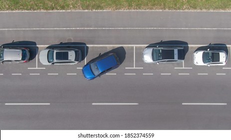 DRONE, TOP DOWN: Flying Above A Shiny Blue Car Driving Out Of A Roadside Parking Space. Modern Vehicle Leaves A Parking Spot In A Long Line Of Parked Cars Next To An Empty City Street In Ljubljana.