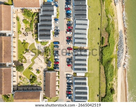 Drone top down view of idyllic holiday chalets and associated parked cars close to a cliff edge on the Suffolk, UK coastline. The North Sea and costal erosion is evident.