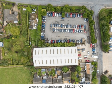 Drone top down view of a large staff car park adjacent to a distribution warehouse in Britain. Private houses adjoin the area on the left.