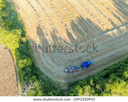 Drone top down view of a tractor and mechanical bailer seen bailing up previously harvested wheat in an English arable field.