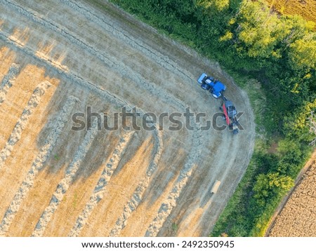Drone top down view of a tractor and mechanical bailer seen bailing up previously harvested wheat in an English arable field.
