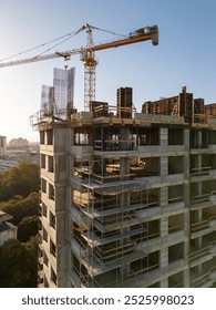 A drone video capturing the construction site of a high-rise building at sunset. The structure's concrete framework, cranes, and scaffolding are bathed in warm sunlight, highlighting urban development