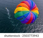 Drone video of a colorful parasail soaring over the open ocean, towed by a speedboat below. The aerial view captures the thrill and freedom of parasailing against a vast, serene seascape