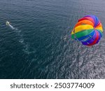 Drone video of a colorful parasail soaring over the open ocean, towed by a speedboat below. The aerial view captures the thrill and freedom of parasailing against a vast, serene seascape