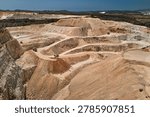 Drone view of an active open pit limestone quarry with terraced excavation levels, haul roads and heavy mining trucks. Industrial mining landscape showing raw material extraction and earthmoving operations.