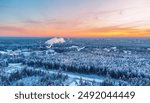 Drone view of a beautiful snow-covered forest in the sunset, away from the city, industrial pipes with smoke.Naure winter landscape