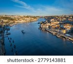 Drone view of Douro River between Porto Ribeira and Vila Nova de Gaia, Portugal, with a tourist boat and moored rabelo boats at sunrise