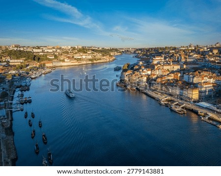 Drone view of Douro River between Porto Ribeira and Vila Nova de Gaia, Portugal, with a tourist boat and moored rabelo boats at sunrise