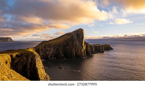 Drone view of dramatic cliffs at Neist Point on Isle of Skye, rugged coastline and distant lighthouse in warm evening light above calm ocean, iconic travel landscape in Scotland
