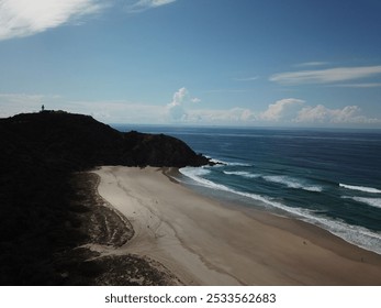 A drone view of an empty beach with blue waters, and a hilltop lighthouse with blue sky in the background in Cape York, Australia - Powered by Shutterstock