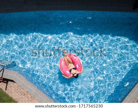 Drone view of a girl laying on a float in private pool