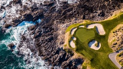 Drone View Of A Golf Course Next To The Ocean With Waves Hitting The Rocks On The Seashore