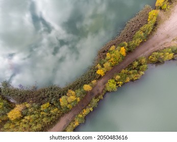 Drone view of a gravel road and trees in autumn colors and turquoise water seen from above. Background with copy space and place for text. Photography taken in September in Sweden.