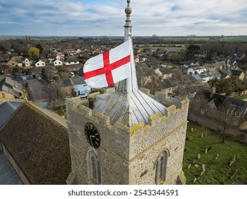 Drone view of a large St Georges flag flying in the wind at the top of a bell tower of a typical English church.