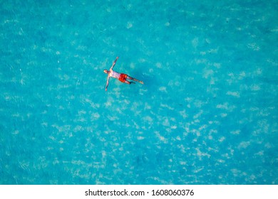 Drone view of a man floating in tropical sea water. Aerial view of young man floating on sea water enjoying sunbathing and vacations in tropical destination. People travel tourism holidays concept. 