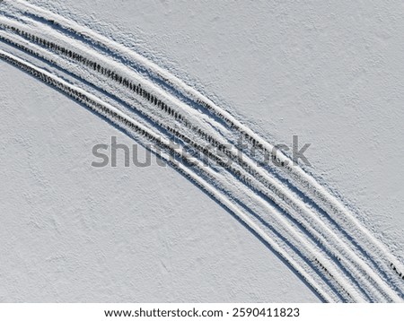 Drone view of parallel tracks on a frozen, snow-covered lake: abstract winter pattern.