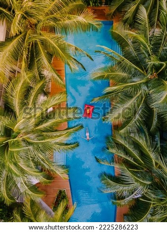 Drone view at the pool with palm trees in a green garden, couple of men and women in swimming pool view from above