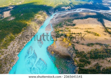A drone view of the river in the mountains valley. An aerial view of an autumn forest. Winding river among the trees. Turquoise mountain water. Landscape with soft light before sunset. 