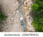 Drone view of riverbank with blue water, green forest and large rocks in riverbed. Top down photo.