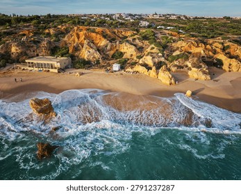 Drone view of waves curling along the beach below golden limestone cliffs at Praia de Sao Rafael beach.