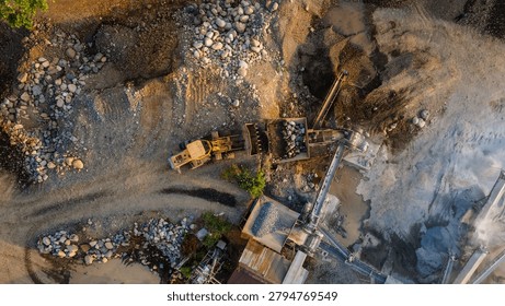 Drone view of a wheel loader operating alongside a rock crusher facility in an active industrial quarry, showcasing aggregate processing and mining activities from above.