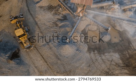 Drone view of a wheel loader operating alongside a rock crusher facility in an active industrial quarry, showcasing aggregate processing and mining activities from above.