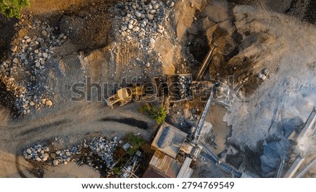 Drone view of a wheel loader operating alongside a rock crusher facility in an active industrial quarry, showcasing aggregate processing and mining activities from above.