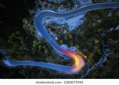 A drone view of a winding mountain road, illuminated by streaks of light from passing cars. Long exposure, dynamics and atmosphere.  