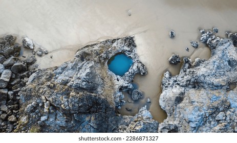 A drone's eye view of the large natural rockpool that gives its name to Blue Pool Bay on the Gower Peninsula in Swansea, UK