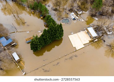 Drone's eye view of spring floodwaters engulfing a riverside beach zone and its amenities. Nature's power evident in the widespread inundation, muddy waters covering structures