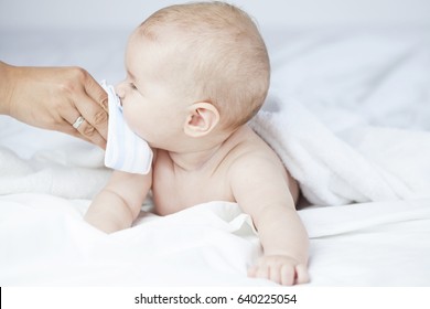 Drooling sick baby with a cold and running nose getting wiped by mom's hand, lying naked in white sheets, Corona virus COVID-19 SARS coronavirus disease quarantine isolation,global pandemic outbreak