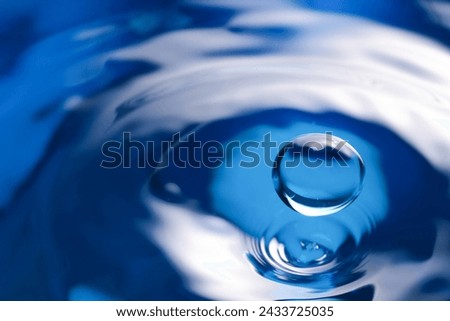 Drop falling into clear water on blue background, closeup