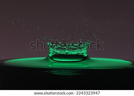 A drop of green water forming a coronet as it splashes into a glass full of liquid, backlit for contrast.