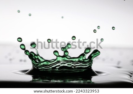 A drop of green water forming a coronet as it splashes into a shallow layer of liquid
