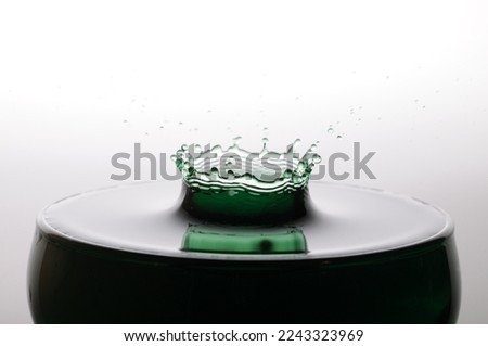A drop of green water forming a coronet as it splashes into a glass full of liquid