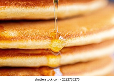 A drop of honey spreads over the pancake.Pancakes with syrup macro shot.Syrup pours on a pancake macro photo.Honey spreads.Drop of syrup close-up.Golden pancakes with glitter syrup.Delicious sweet  - Powered by Shutterstock