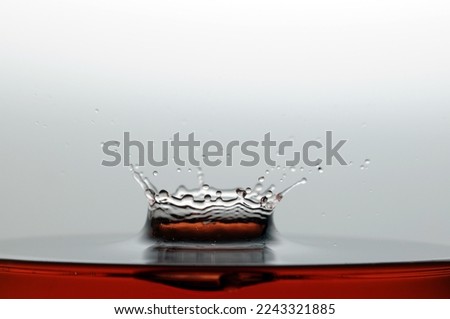 A drop of orange water forming a coronet as it splashes into a glass full of liquid, backlit for contrast.