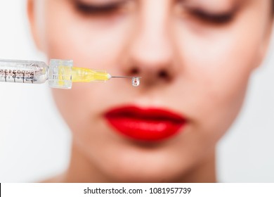 A drop of preparation hangs from the needle of the syringe against the face of the patient. Macro close upA drop of Botox hangs from the needle of the syringe against the face of the patient. Macro