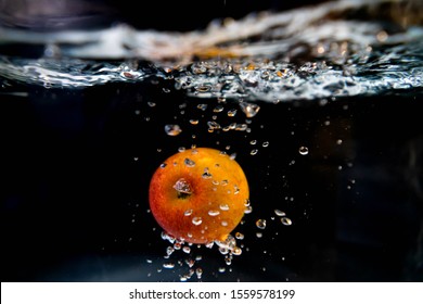 Drop Red Apple In Tank. Water Is Splash On Black Background