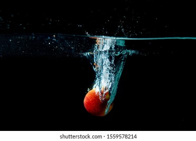 Drop Red Apple In Tank. Water Is Splash On Black Background