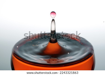 A drop of red water forming a column as it splashes into a glass full of liquid, backlit for contrast.